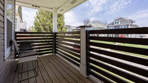 Une véranda couverte avec un plancher en bois, une rambarde en métal et un banc.