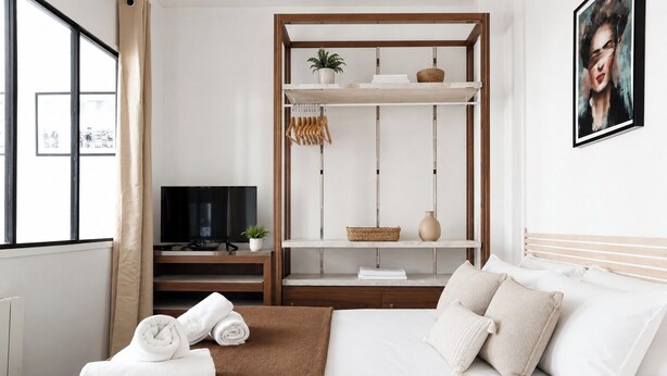 A bedroom with a bed, a TV, a shelf with decorative items, and a window with curtains. - TheBlueStay 350 - Stunning Apt in République (Paris)
