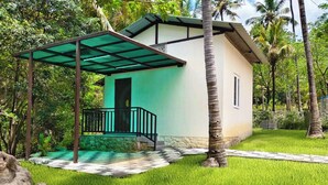 A small house with a covered porch, surrounded by lush greenery and palm trees. - Heaven In Woods (Mekkarai)