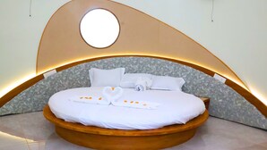 A circular bed with a wooden frame, white bedding, and a floral-patterned headboard. - Heaven In Woods (Mekkarai)