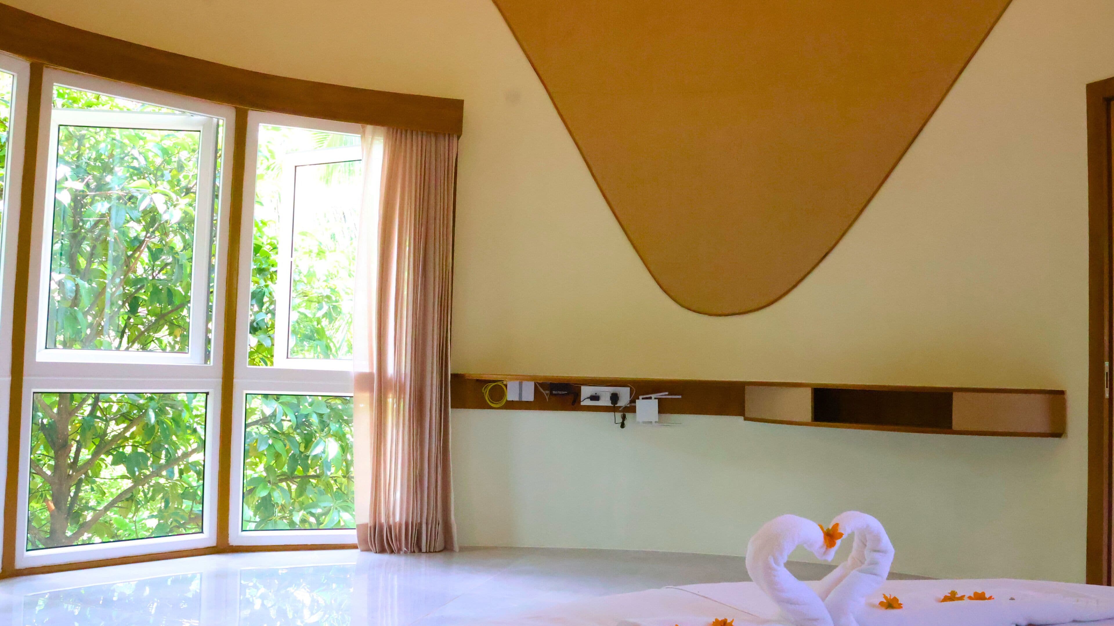 Quarto com janelas amplas, cama com lençóis brancos e decoração de toalha em formato de coração.