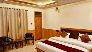 Habitación de hotel con techo de madera, una cama grande, dos sillas, una mesita y una puerta.
