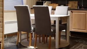A compact kitchen with a dining table and chairs, wooden cabinets, and a window with blinds. - Cozy 2-bedroom cabin in peaceful Gryllefjord with AC (GRYLLEFJORD)