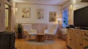 A living room with a fireplace, two armchairs, a coffee table, a TV, and wall art. - Cozy 2-bedroom cabin in peaceful Gryllefjord with AC (GRYLLEFJORD)