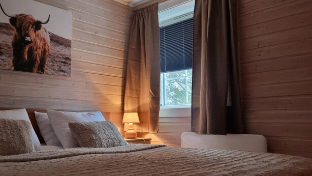 A bedroom with a wooden headboard, a bed with multiple pillows, a nightstand with a lamp, and a large painting of a bull on the wall. - Cozy 2-bedroom cabin in peaceful Gryllefjord with AC (GRYLLEFJORD)
