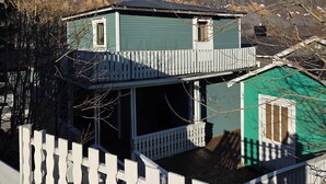A two-story house with a balcony, surrounded by a white picket fence, set against a mountainous backdrop. - Cozy 2-bedroom cabin in peaceful Gryllefjord with AC (GRYLLEFJORD)