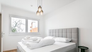 Een moderne slaapkamer met een groot bed, een raam met uitzicht op gebouwen en een groen nachtkastje.