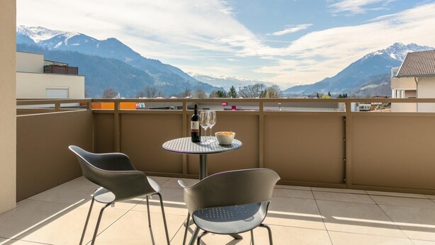 Een balkon met een tafel, twee stoelen, een fles wijn en een schaal met snacks.