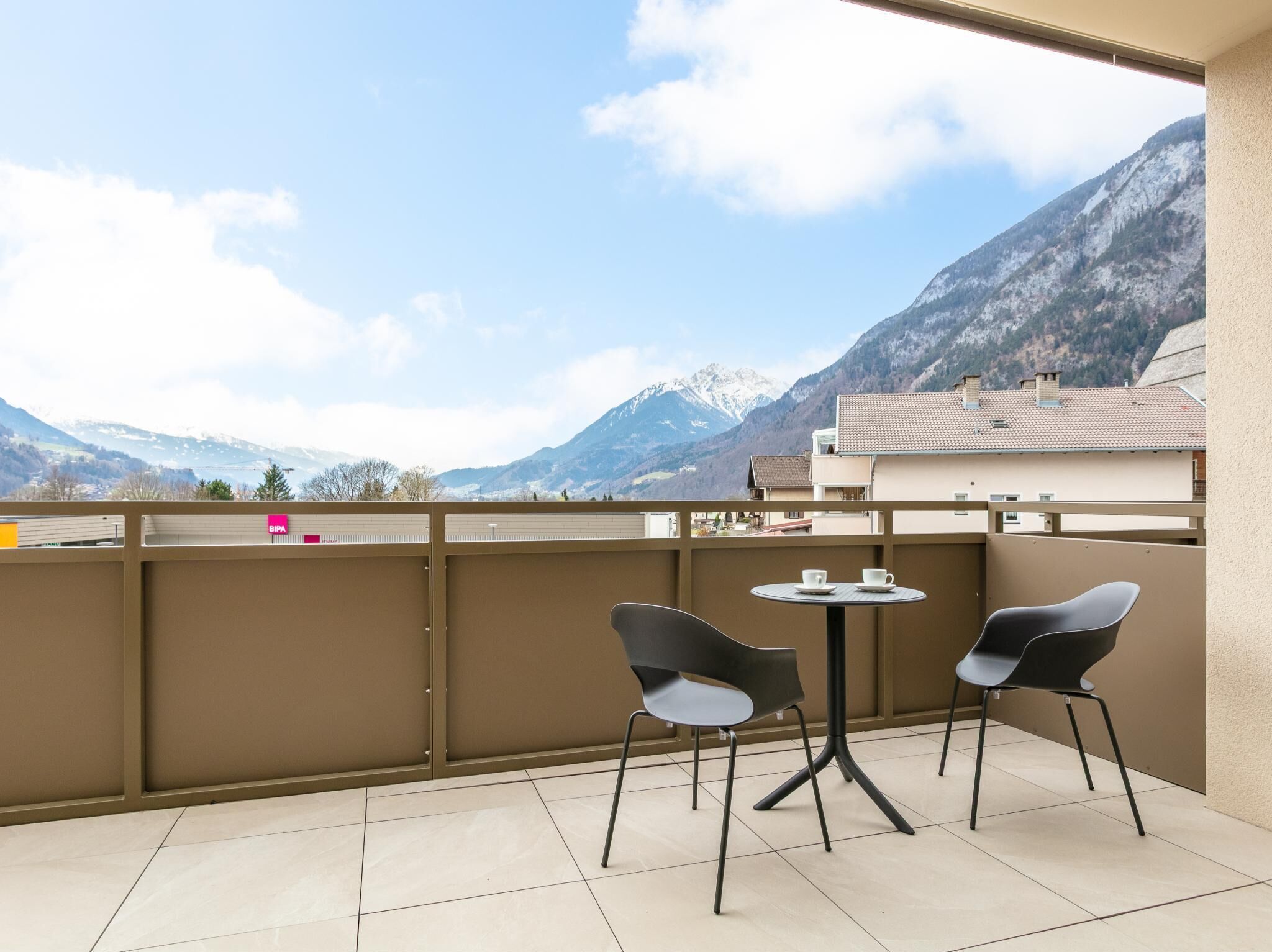Ein Balkon mit zwei Stühlen und einem Tisch, mit Blick auf eine gebirgige Landschaft.