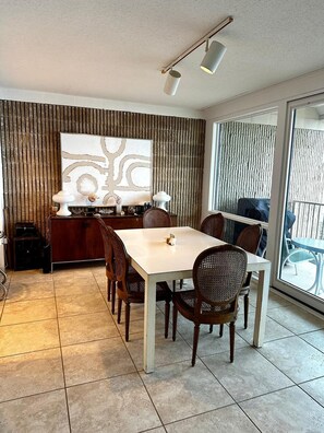A dining area with a white table, wicker chairs, a decorative wall, and a large window. - 21 Ocean Drive unit 902- Water Views in the North Shores Community. (Rehoboth Beach)