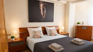 Ein Schlafzimmer mit Bett, Nachttischen, einem Schminktisch und einem Deckenventilator, sowie einer Buddha-Statue.