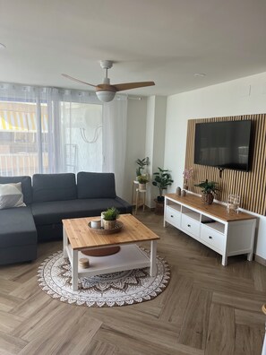 Ein modernes Wohnzimmer mit einer Couch, einem Couchtisch, einem Fernseher und einem Deckenventilator.