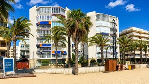 Ein Hotel direkt am Strand mit mehreren Balkonen, Palmen und einem strahlend blauen Himmel.
