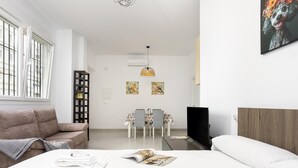 A modern hotel room with a bed, a sofa, a dining table with chairs, a TV, and artwork on the walls. - Sunstay Luzon Loft I Málaga (Málaga)
