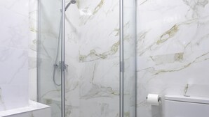 A bathroom with a glass-enclosed shower, marble walls, a white toilet, and a towel on a surface. - Sunstay Luzon Loft I Málaga (Málaga)