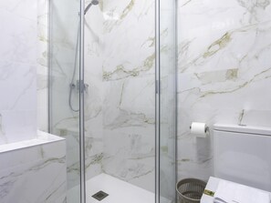 Ein Badezimmer mit einer gläsernen Duschkabine, Marmorwänden, einer weißen Toilette und einem Handtuch auf einer Ablagefläche.