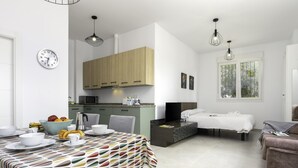 A modern kitchen with wooden cabinets, a dining area with a colorful tablecloth, and a bedroom with a bed and window. - Sunstay Luzon Loft I Málaga (Málaga)