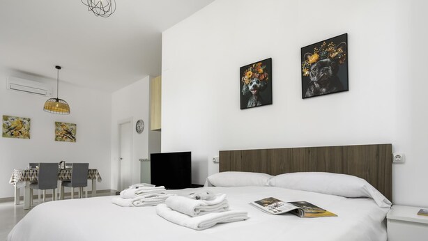 A modern hotel room with a large bed, a flat-screen TV, a dining area with a table and chairs, and artwork on the walls. - Sunstay Luzon Loft I Málaga (Málaga)