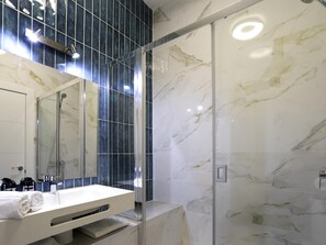 Ein modernes Badezimmer mit einer Duschkabine aus Glas, einem weißen Waschbecken und einem großen Spiegel.