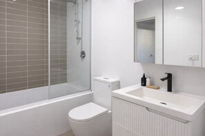 A modern bathroom with a glass-enclosed shower, a white toilet, and a sink with a mirror above. - Warm & Convenient Home Near the Lake in Pemulwuy (Pemulwuy)