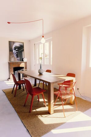 Un comedor con una mesa larga, sillas rojas, un florero y una lámpara colgante.