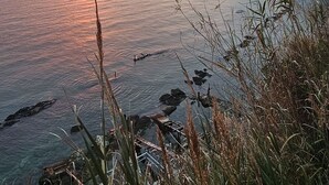 Sonnenuntergang an der Küste mit Klippen und Vegetation.