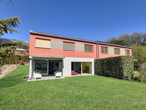Een modern herenhuis met twee verdiepingen, een rode gevel, grote schuifdeuren van glas en een verzorgd gazon.