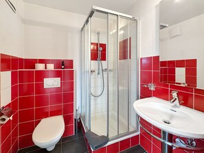 Een badkamer met een douchecabine van glas, een witte wastafel en een toilet.