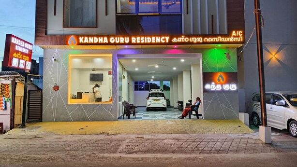 A building with a sign reading 'Kandha Guru Residency' and a car parked in front.