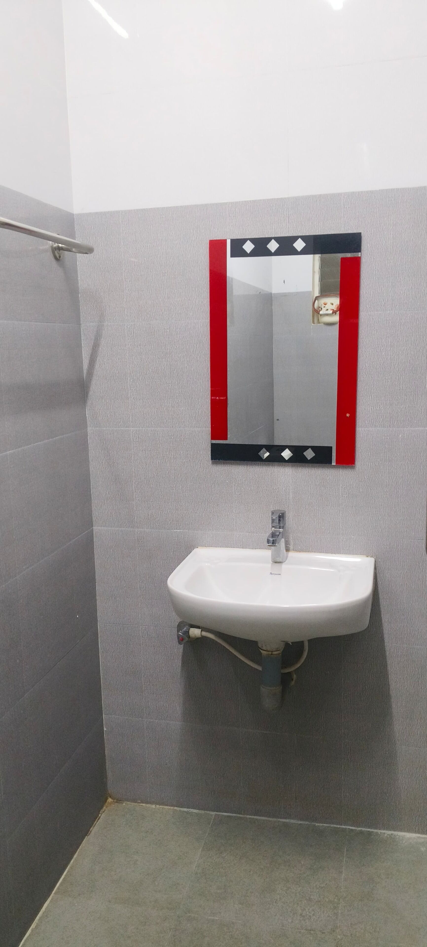 Une salle de bain avec un lavabo blanc, un miroir à cadre rouge et des murs recouverts de carreaux gris.