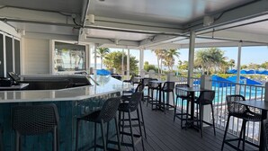 A covered outdoor bar area with a pool view, bar stools, and a counter. - Beachfront 2BR Condo at Casa Ybel Resort: Corner Unit, Patio-to-Beach Walk-Out (Sanibel)