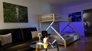 Ein Etagenbett mit einer Leiter, ein Glastisch, ein schwarzes Sofa und ein Bild an der Wand.