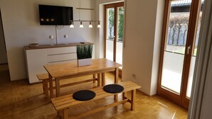 Moderni keittiö, jossa on puinen pöytä, penkkimäinen istuinjärjestely ja seinälle asennettu litteänäyttöinen televisio, joka on sijoitettu työtason yläpuolelle.