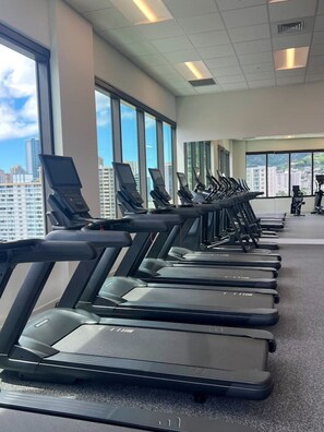 A row of treadmills in a gym with large windows and a city view. - High-Rise Retreat | Panoramic Ocean & City Views (Honolulu)