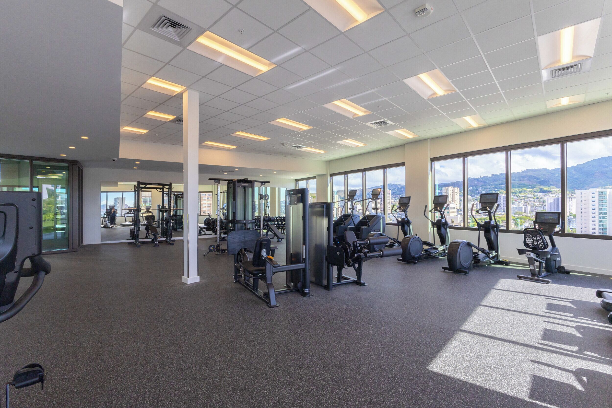 A gym with various exercise equipment, large windows, and a city view.