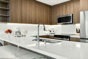 A modern kitchen with a white countertop, stainless steel appliances, and wooden cabinetry. - High-Rise Retreat | Panoramic Ocean & City Views (Honolulu)