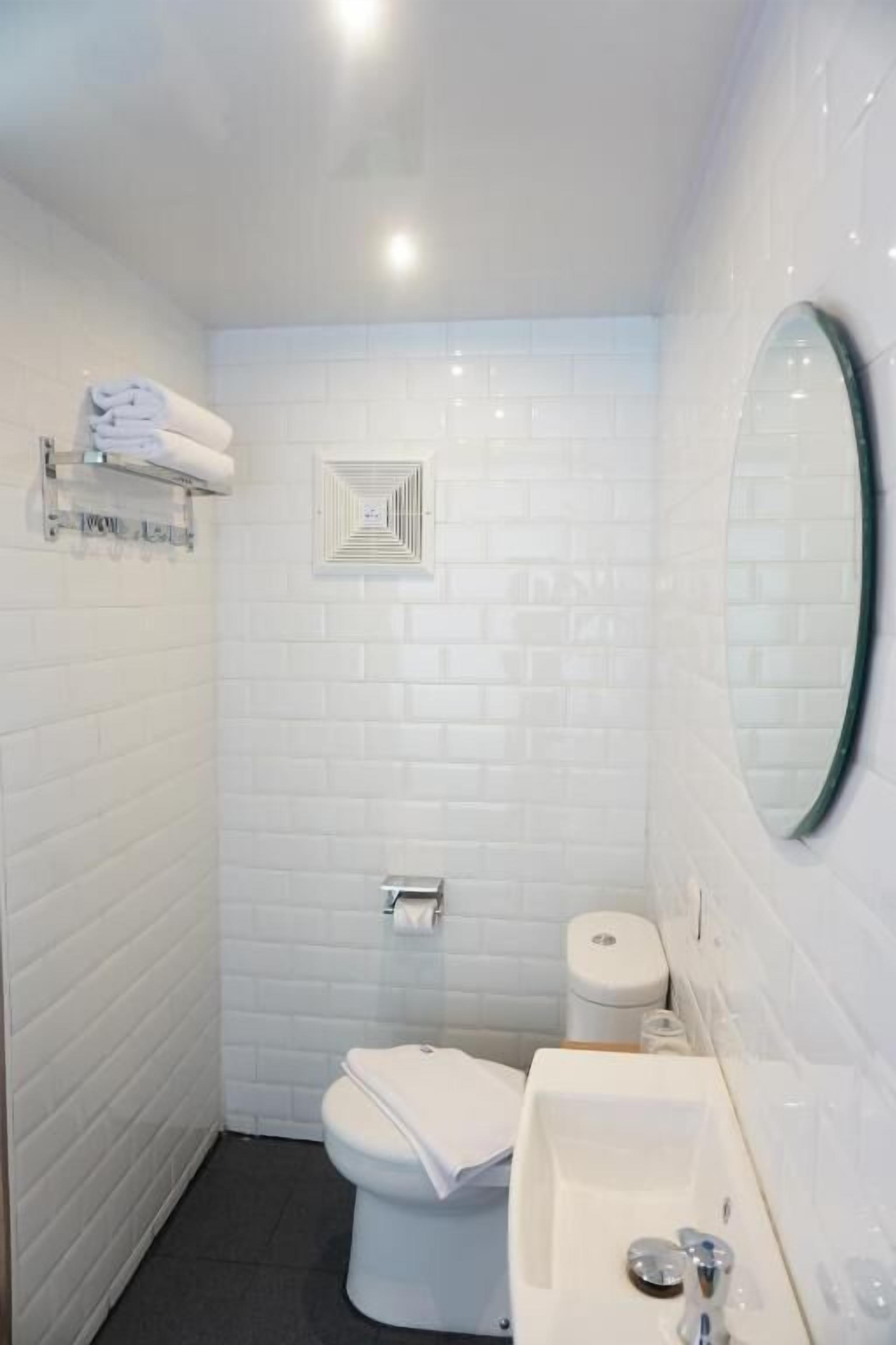 A bathroom with white tiled walls, a white toilet, a sink with a mirror, and a towel rack.