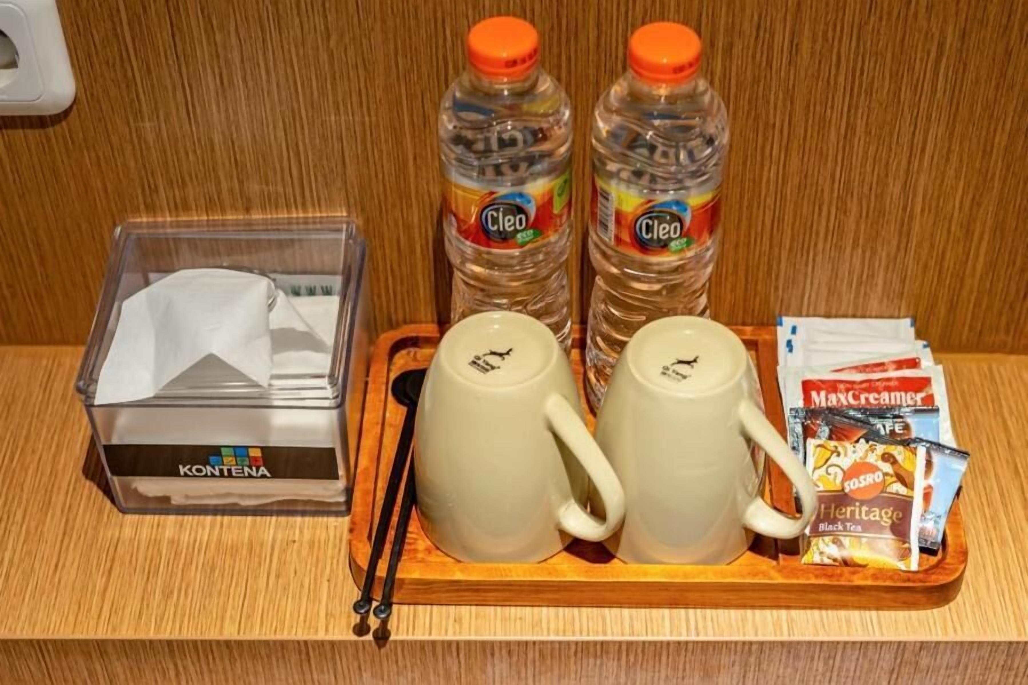 Een dienblad met twee waterflesjes, twee witte mokken, een paar stokjes, een zak tissues en een pakje MaxCreamer.