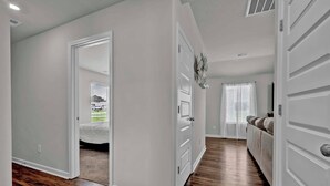 A hallway with hardwood flooring, white walls, and a door leading to a bedroom.