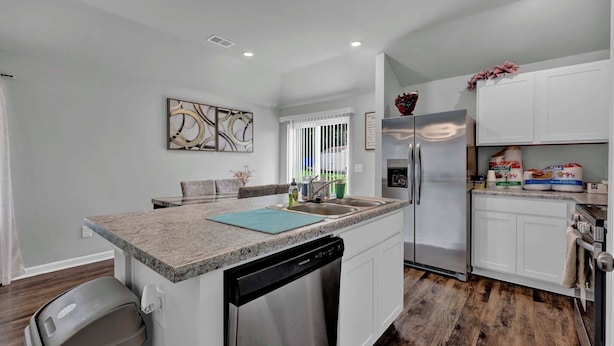 A modern kitchen with white cabinetry, a granite countertop, a dishwasher, a refrigerator, and a dining area with a table and chairs.