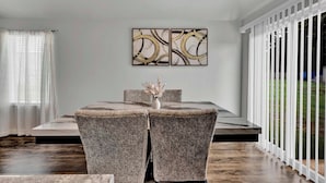 A dining area with a glass table, two upholstered chairs, and a wall-mounted abstract art piece.