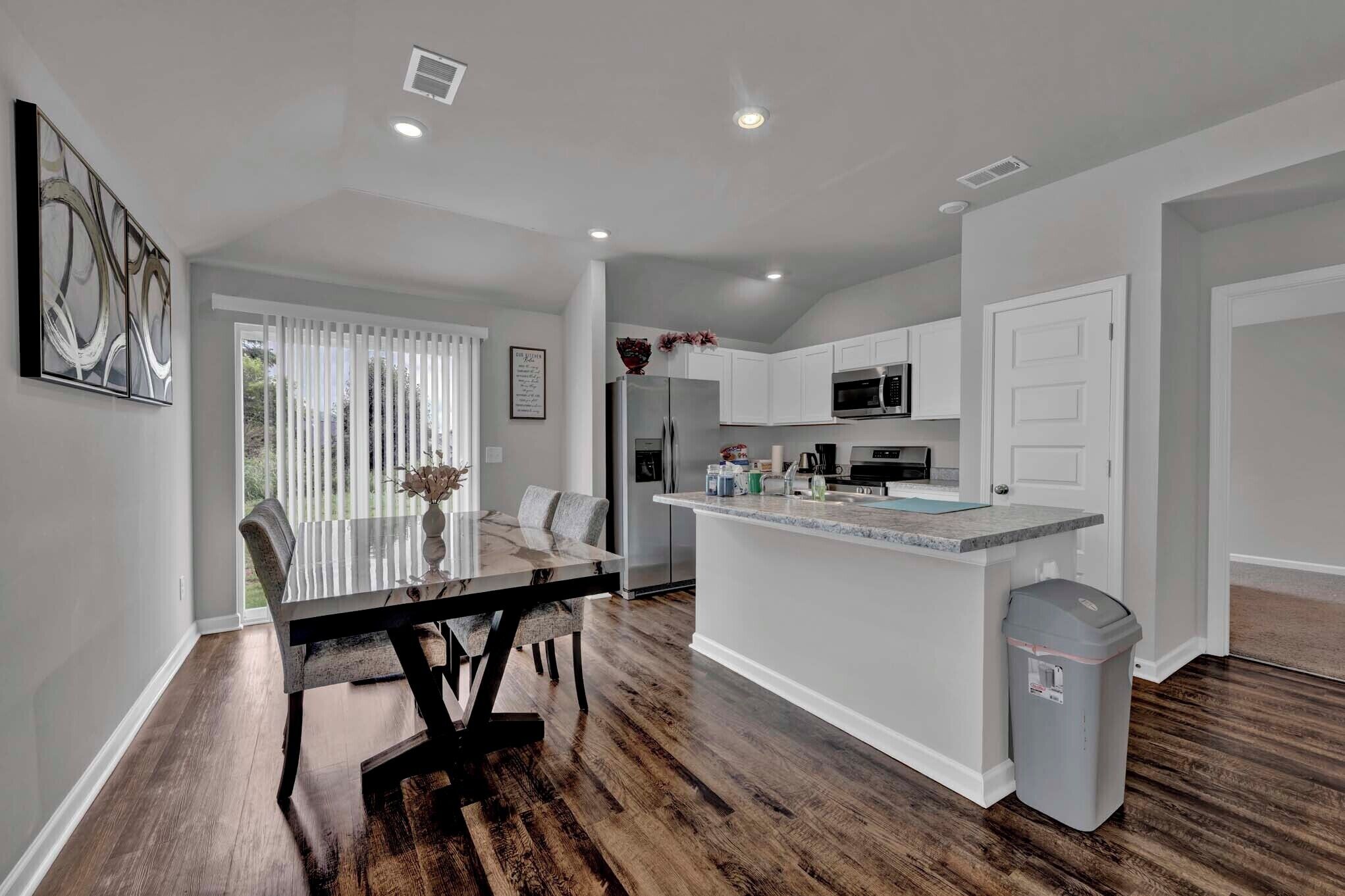 A modern kitchen with white cabinets, a central island, and a dining area with a glass table.