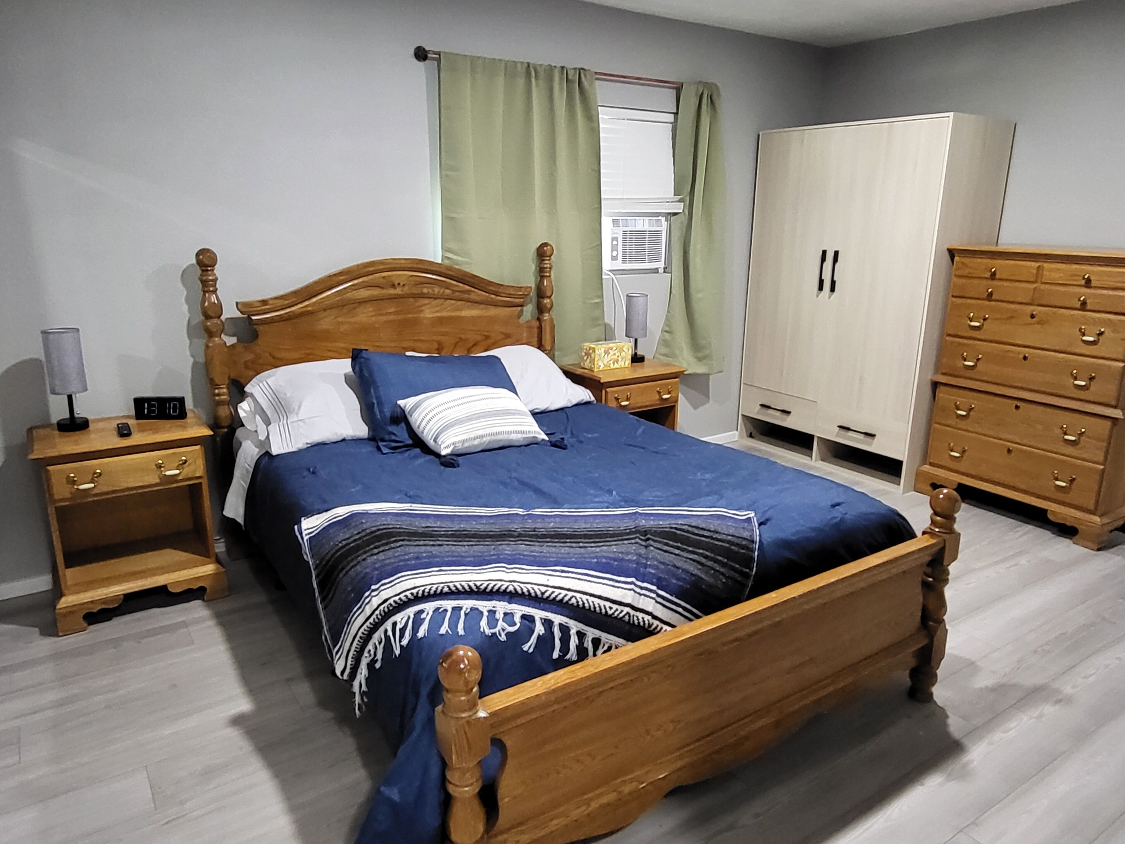 A bedroom with a wooden bed, a nightstand with a lamp, a dresser, and a wardrobe.