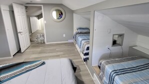 Un dormitori amb un llit superposat, un llit individual, un mirall, un ventilador i una porta que dona a una altra habitació.