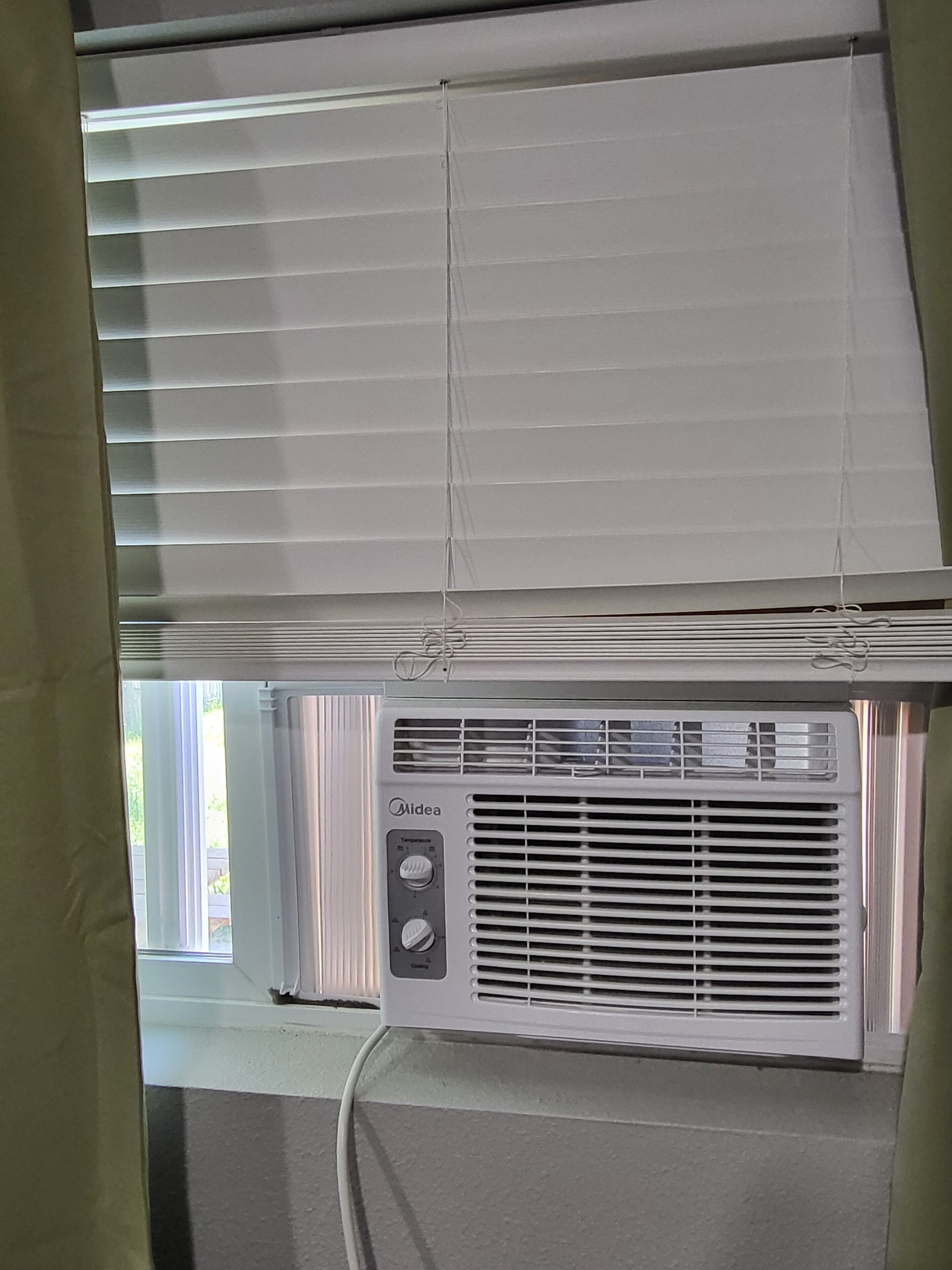 A room with a window, a wall-mounted air conditioning unit, and a curtain.