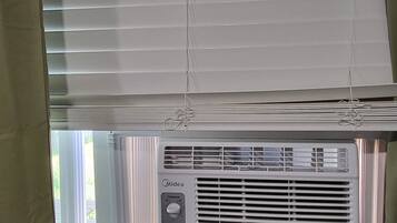 A room with a window, a wall-mounted air conditioning unit, and a curtain.
