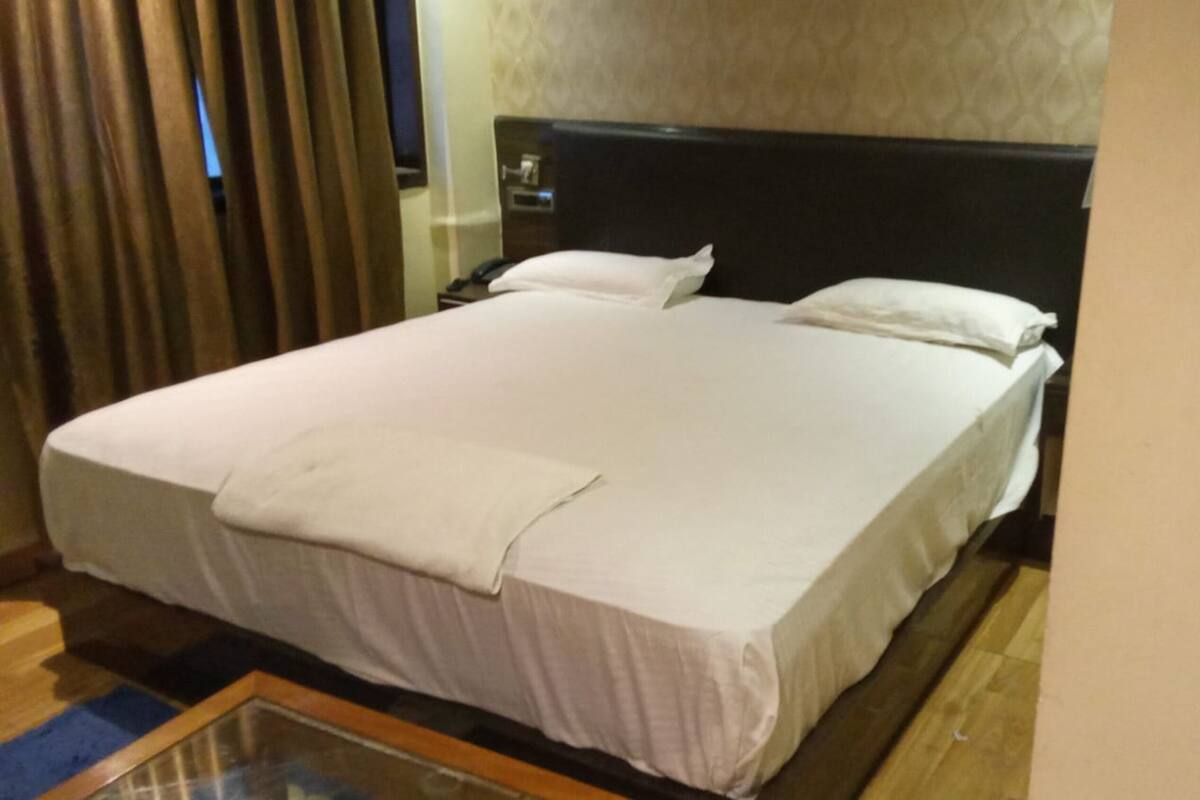 Habitación de hotel con una cama grande, una mesita de noche, un espejo y una ventana con cortinas.