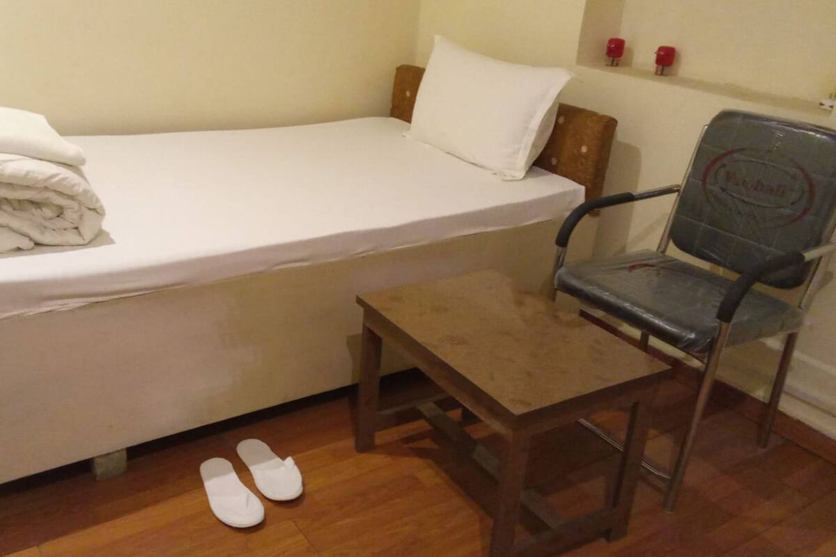 Una habitación pequeña con cama individual, una silla de madera y un par de zapatillas en el suelo.
