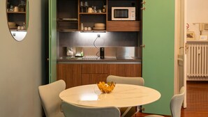 A compact kitchen with a microwave, shelves with dishes, and a dining area with a table and chairs. - Crocetta Golden Soul | Design Loft near Porta Nuova (TORINO)