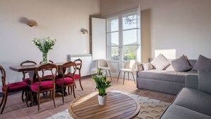 A living room with a wooden dining table, red upholstered chairs, a grey sofa, and a potted plant on a round wooden coffee table. - Cosy apartment in villa for 6 guests with WIFI, pool and TV, close to Greve In Chianti (Badia A Passignano)